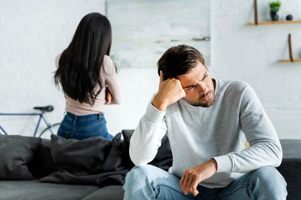 Selective focus of sad and handsome man and african american woman sitting on sofa