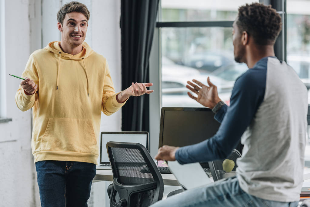 Two young multicultural programmers gesturing during discussion in office