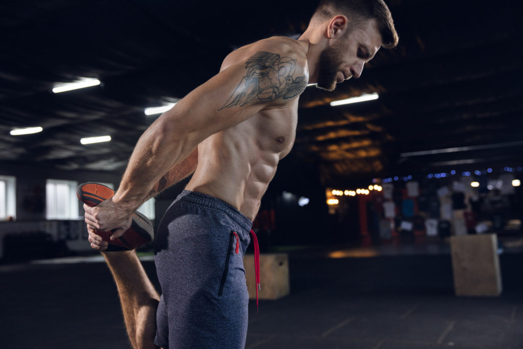 Young healthy man doing exercises, stretching in gym