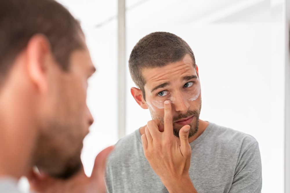 Man putting under eye cream on face taking care of his skin