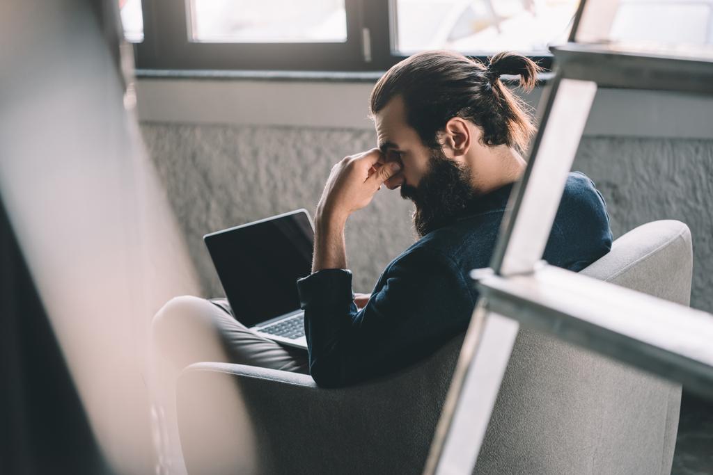Thoughtful businessman working with laptop in armchair
