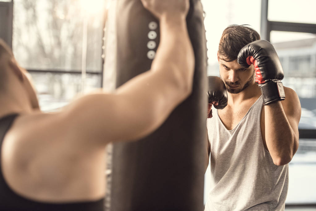 trainer holding punching bag while boxer training in gym