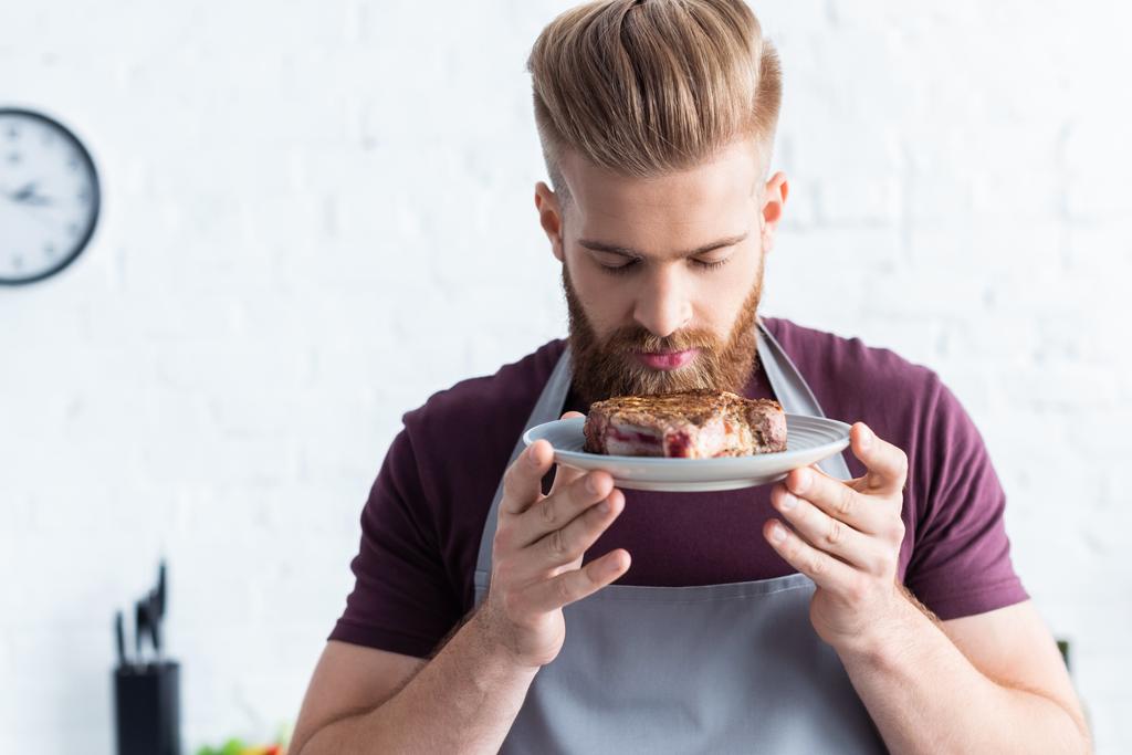 man in apron holding plate with delicious beef steak