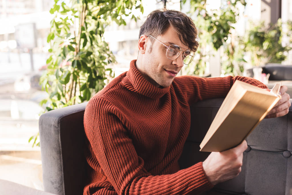 Handsome man in glasses reading book while sitting in cafe