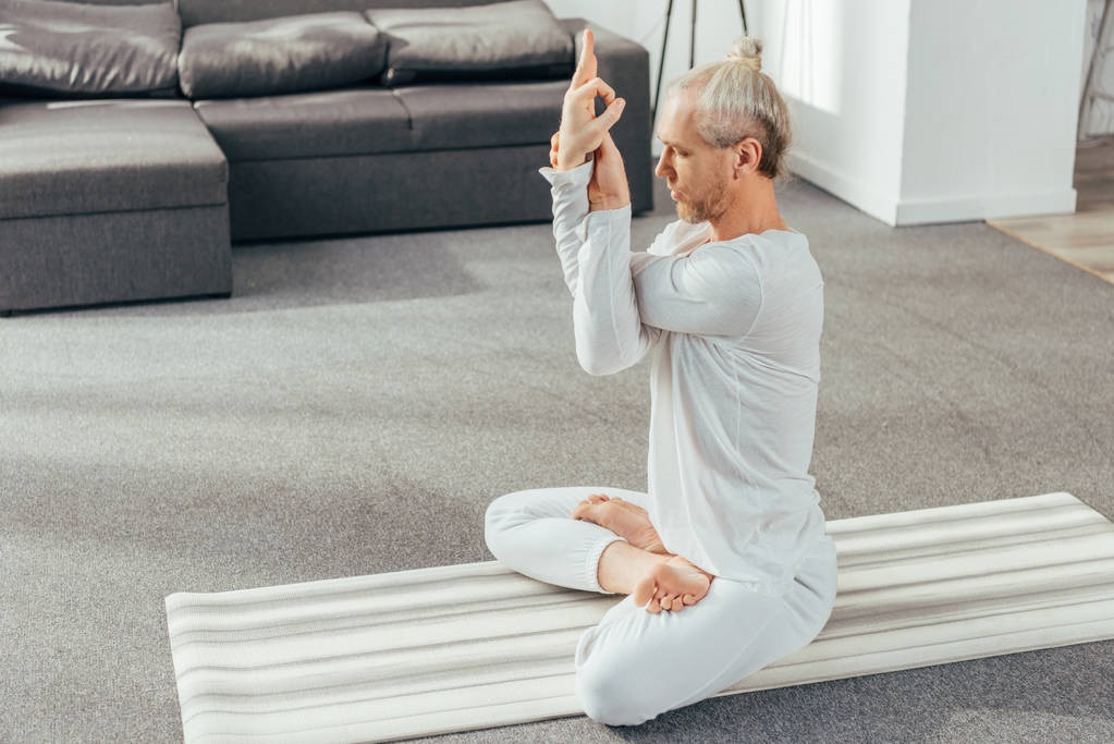 man meditating in lotus position with mudra sign at home 