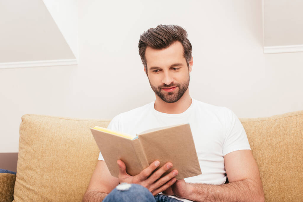 handsome man reading book on couch in living room