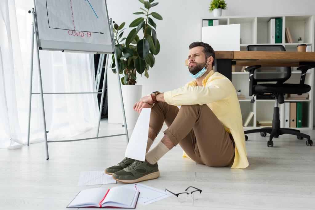 man sitting on floor and looking away near papers