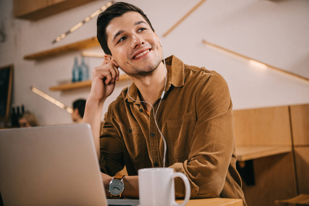 man in earphones listening music near laptop in cafe