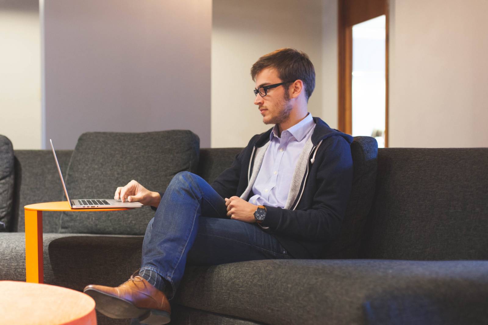 Royalty-Free photo: Man in black zip-up jacket and blue denim jeans sitting on sofa