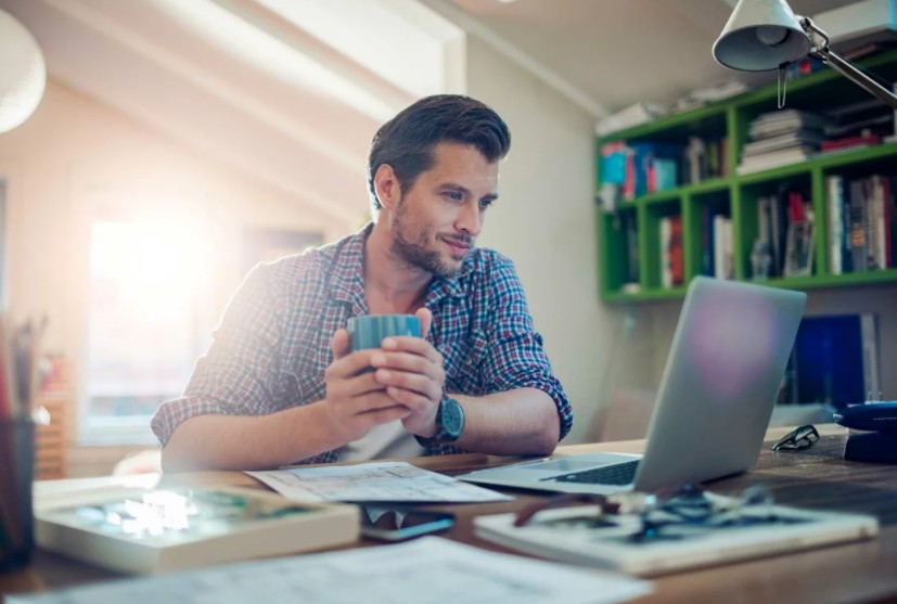 man holding cup and looking at laptop screen 