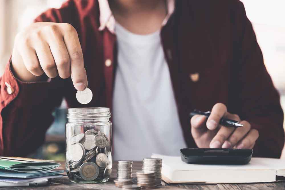 Man hand putting money (coin) in the glass jar during use calculator for calculate income