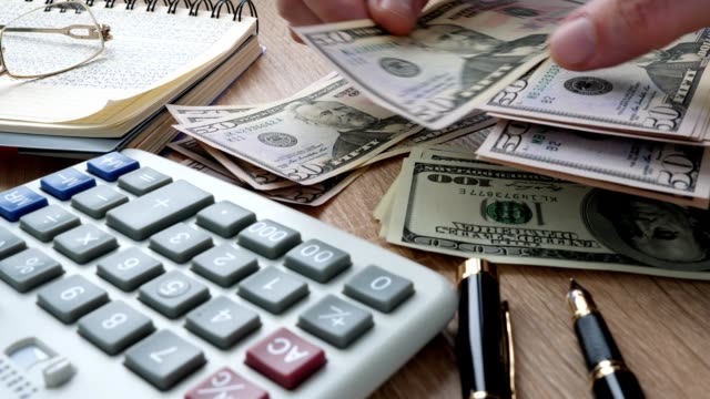 Man counting money on an office desk. Dollar bills and calculator