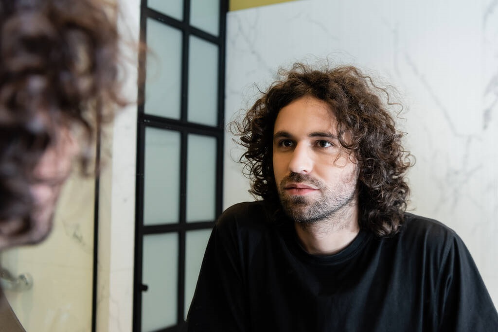 handsome curly man looking at mirror in bathroom