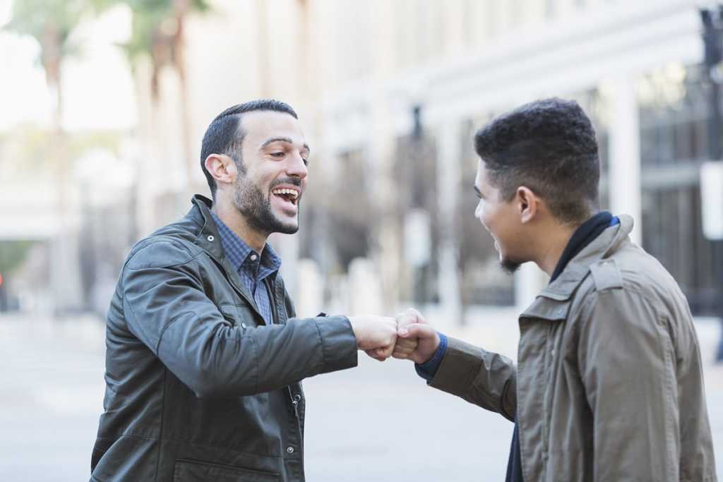 Two Young Men Greeting On City Street With Fist Bump