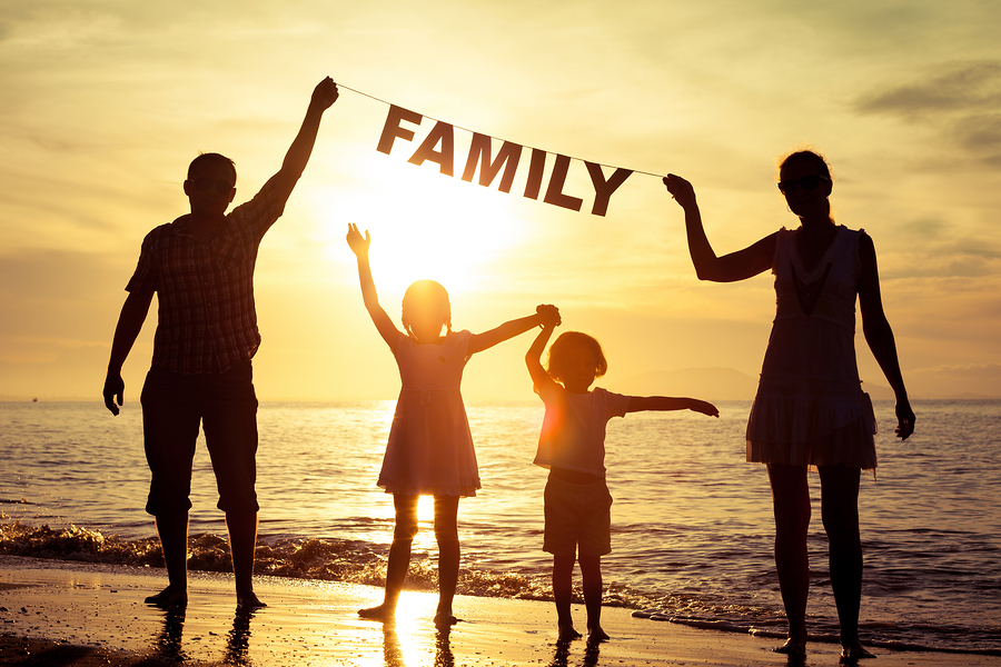 Happy family standing on the beach at the sunset time