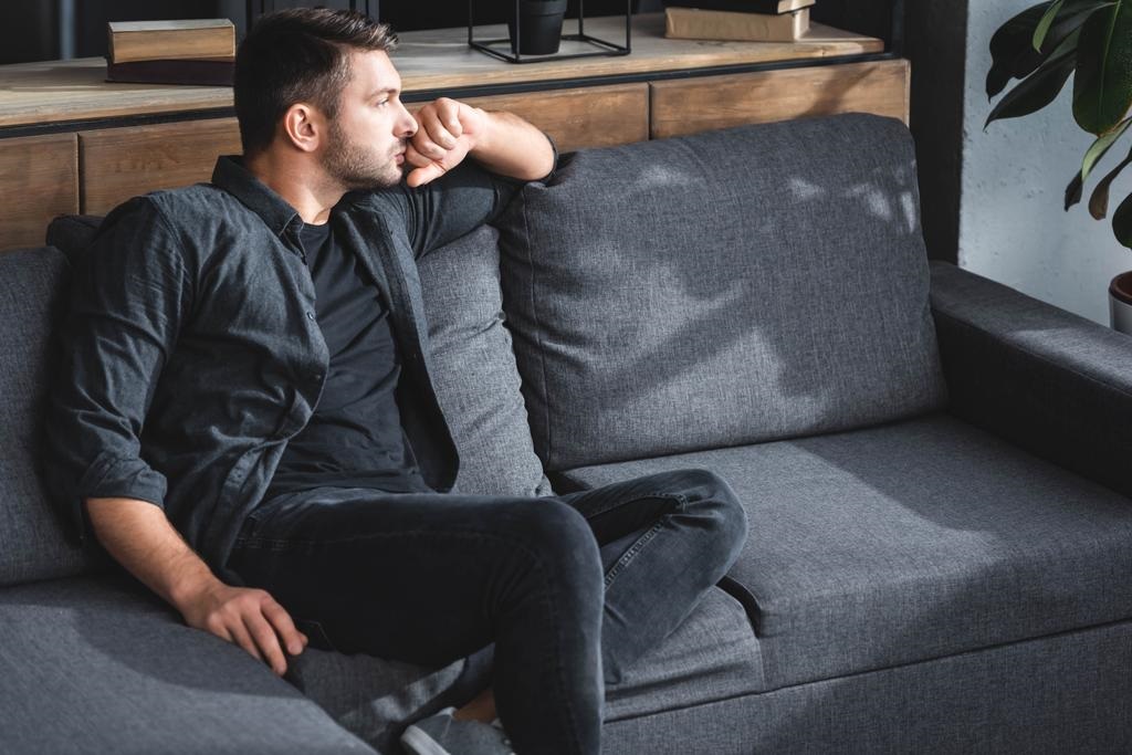 Handsome And Pensive Man Sitting On Sofa 
