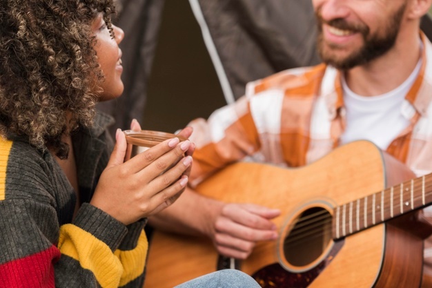 Couple playing guitar while camping outside
