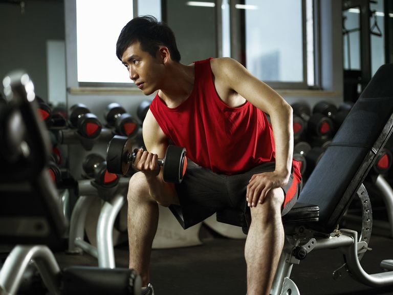 man-sitting-on-weight-bench-lifting-dumb-bells